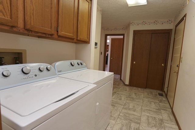 laundry room featuring cabinet space, a textured ceiling, and washer and clothes dryer