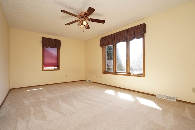 empty room with visible vents, a ceiling fan, a textured ceiling, carpet flooring, and baseboards