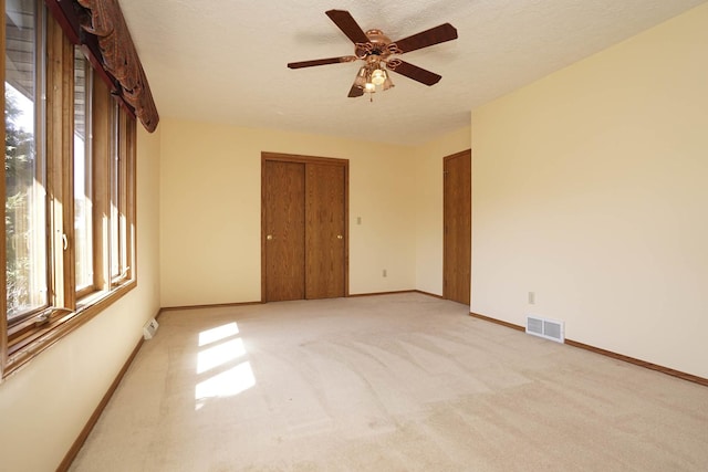 spare room with visible vents, light colored carpet, a textured ceiling, and baseboards