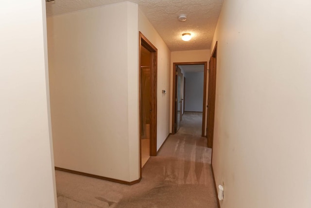 corridor featuring baseboards, light colored carpet, and a textured ceiling