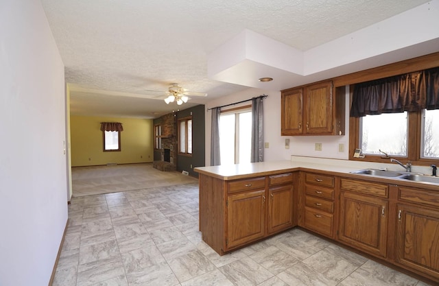 kitchen with a peninsula, a sink, light countertops, open floor plan, and brown cabinets