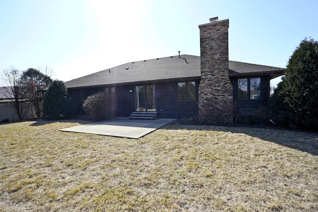 back of house with a yard, roof with shingles, a chimney, and a patio area