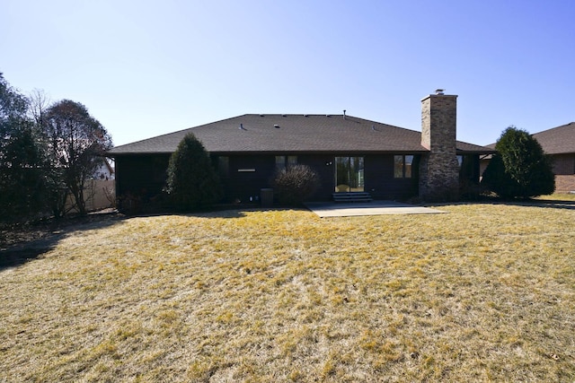 rear view of property featuring a patio area, a lawn, a chimney, and roof with shingles