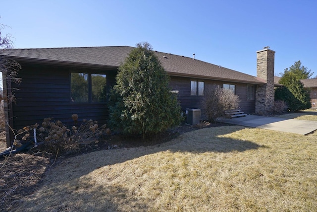 back of house featuring a lawn, a chimney, central AC, and roof with shingles