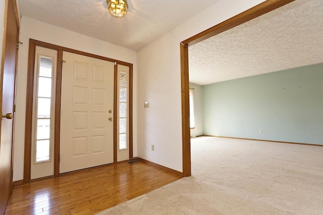 foyer featuring baseboards, a textured ceiling, carpet floors, and wood finished floors