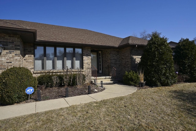 view of front of property featuring brick siding and roof with shingles