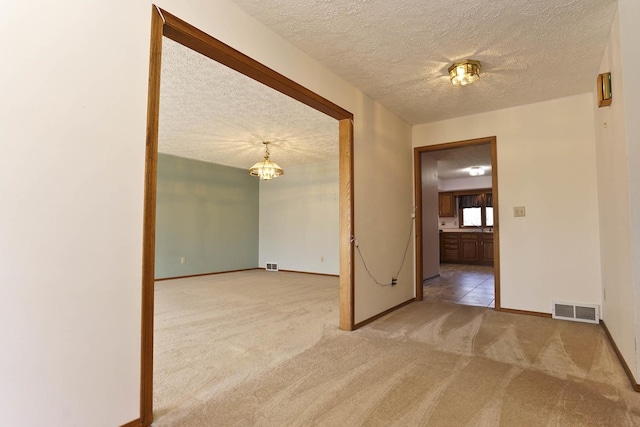 carpeted empty room featuring an inviting chandelier, baseboards, visible vents, and a textured ceiling