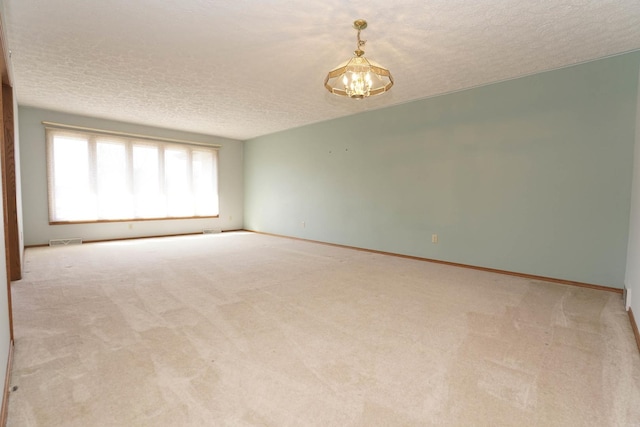 carpeted spare room with visible vents, baseboards, a notable chandelier, and a textured ceiling