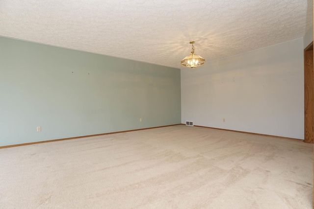 empty room featuring visible vents, light colored carpet, an inviting chandelier, and a textured ceiling