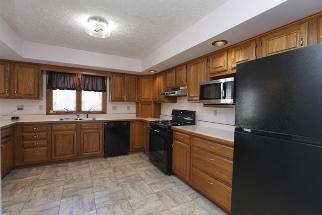 kitchen with under cabinet range hood, light countertops, brown cabinetry, black appliances, and a sink