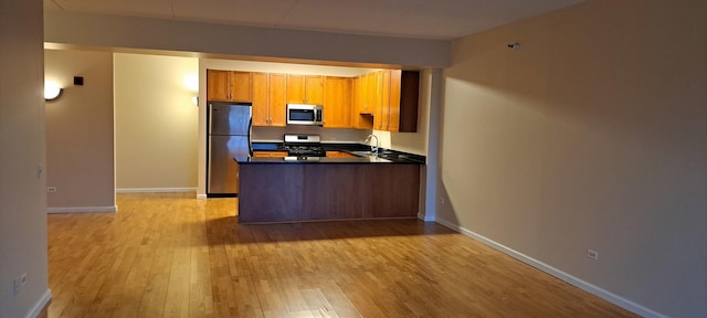 kitchen with a sink, dark countertops, stainless steel appliances, light wood-style floors, and a peninsula