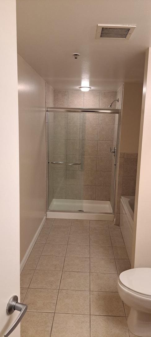 full bathroom featuring tile patterned floors, toilet, visible vents, and tiled shower