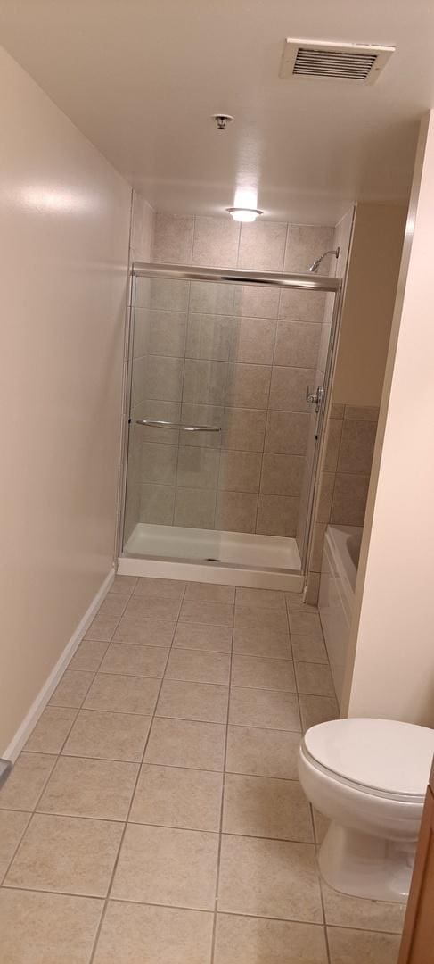 bathroom with tile patterned flooring, toilet, visible vents, and tiled shower