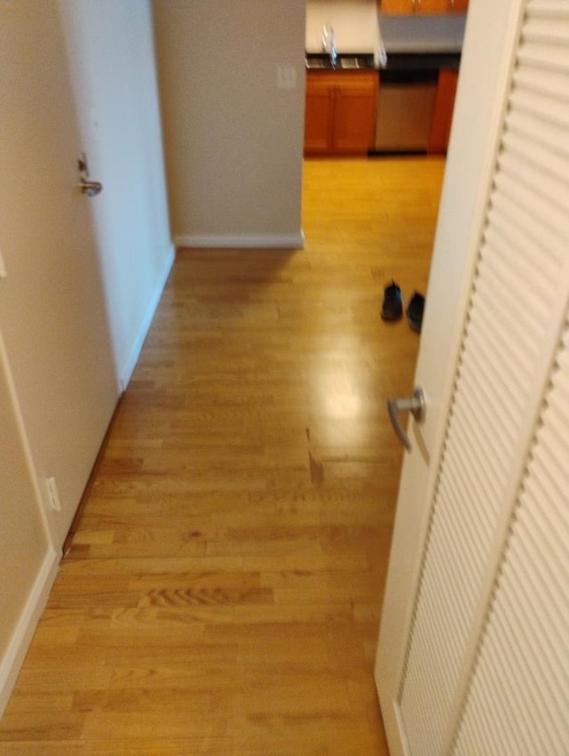 hallway featuring baseboards, light wood-type flooring, and a sink