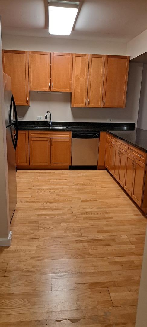 kitchen featuring light wood finished floors, stainless steel appliances, dark countertops, and a sink