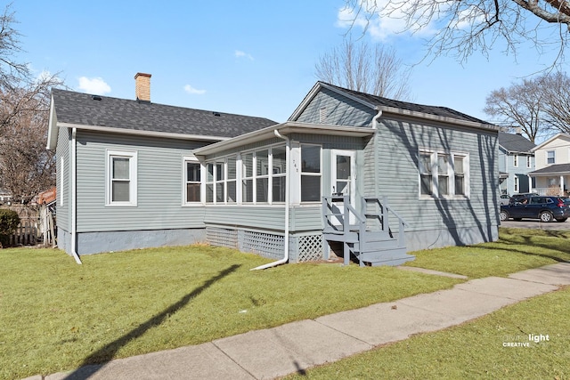 view of front of house with a front yard, roof with shingles, a sunroom, a chimney, and entry steps