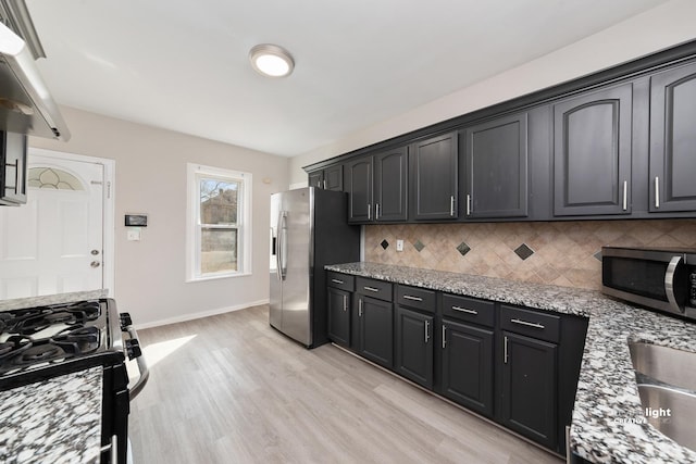 kitchen with light stone countertops, baseboards, light wood finished floors, stainless steel appliances, and backsplash