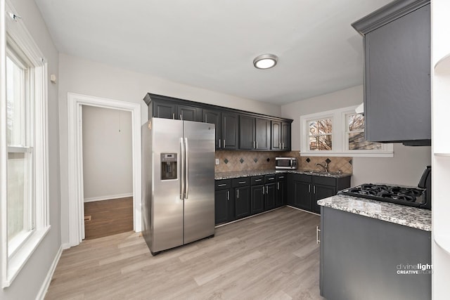 kitchen featuring baseboards, light wood-type flooring, light stone counters, decorative backsplash, and appliances with stainless steel finishes