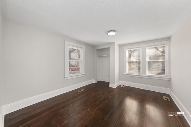 unfurnished bedroom featuring multiple windows, dark wood-style floors, baseboards, and a closet