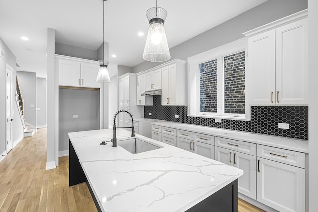 3308 S Leavitt St, Chicago, IL 60608 - kitchen with white cabinets, light wood finished floors, under cabinet range hood, a sink, and backsplash