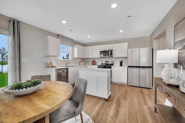 kitchen featuring light wood-type flooring, a sink, a center island, appliances with stainless steel finishes, and white cabinets