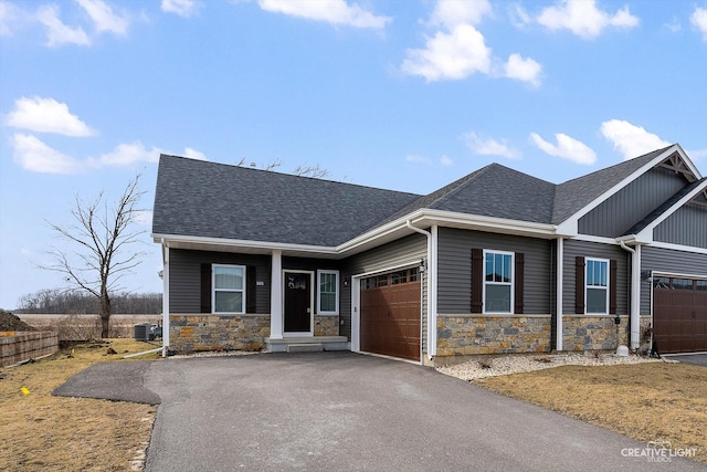 craftsman inspired home featuring driveway, roof with shingles, a garage, stone siding, and central air condition unit