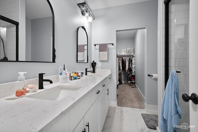 full bath with a walk in closet, marble finish floor, a sink, a tile shower, and double vanity