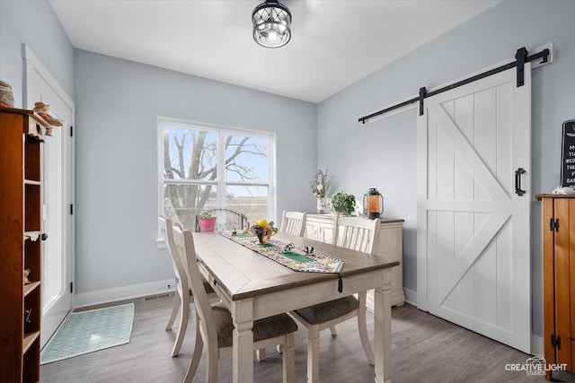 dining space featuring a barn door, baseboards, visible vents, and wood finished floors