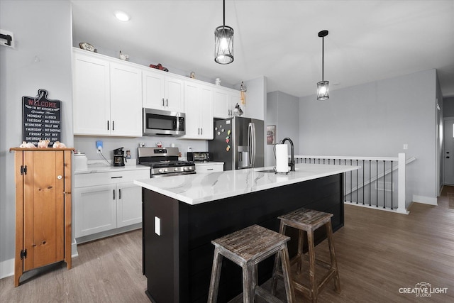 kitchen with an island with sink, a sink, wood finished floors, stainless steel appliances, and white cabinets