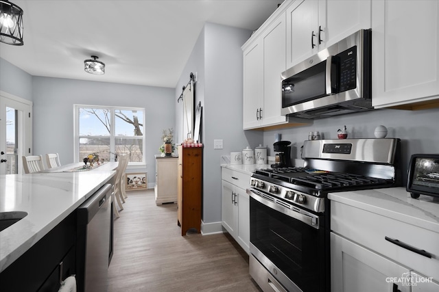 kitchen with light stone countertops, a barn door, appliances with stainless steel finishes, wood finished floors, and white cabinets