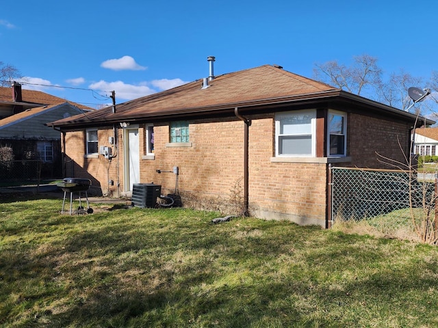 back of property featuring a yard, brick siding, central AC unit, and fence