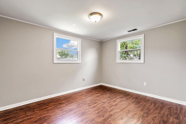 empty room with a healthy amount of sunlight, dark wood finished floors, and crown molding