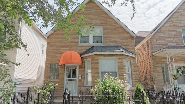 view of front of property featuring fence, stone siding, and roof with shingles