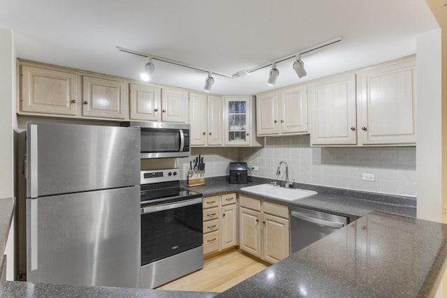 kitchen with dark countertops, track lighting, a sink, stainless steel appliances, and decorative backsplash
