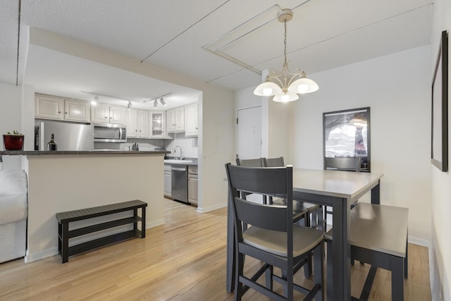 dining room with light wood-style floors, baseboards, rail lighting, and a notable chandelier