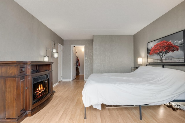 bedroom featuring light wood-type flooring, baseboards, a warm lit fireplace, and a spacious closet