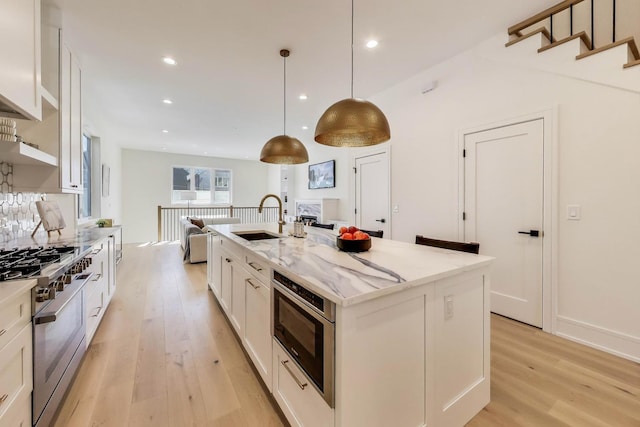 kitchen with a center island with sink, light wood-style flooring, white cabinets, high end stainless steel range, and a sink