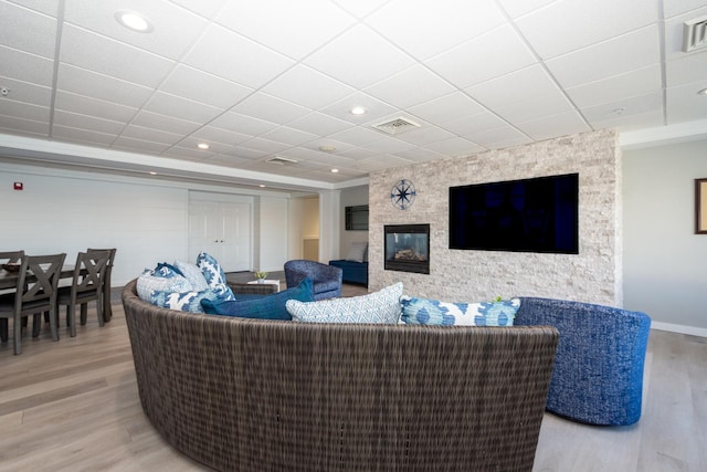 living area with wood finished floors, visible vents, a drop ceiling, and a large fireplace