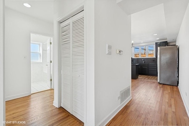 hallway featuring visible vents, baseboards, and light wood-style flooring