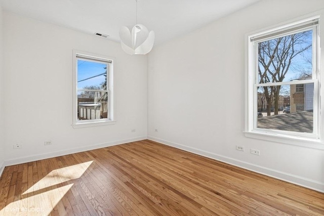 empty room with hardwood / wood-style flooring, visible vents, and baseboards