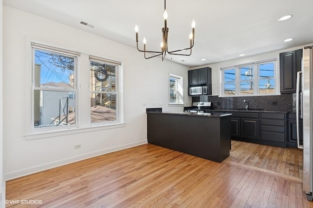 kitchen featuring light wood finished floors, visible vents, baseboards, decorative backsplash, and stainless steel appliances