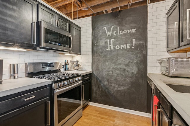 kitchen with backsplash, baseboards, light countertops, light wood-style flooring, and appliances with stainless steel finishes