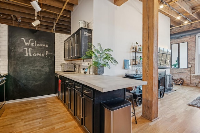 kitchen featuring track lighting, brick wall, beam ceiling, light wood-style flooring, and a kitchen breakfast bar