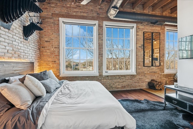 bedroom featuring multiple windows, wood finished floors, and brick wall