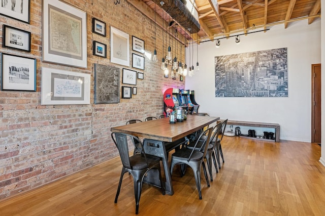 dining space with beam ceiling, wood ceiling, wood finished floors, and brick wall