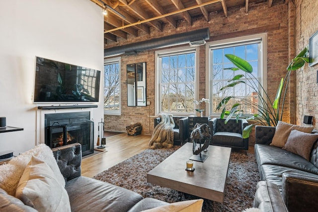 living area with beam ceiling, a warm lit fireplace, wood finished floors, brick wall, and wood ceiling