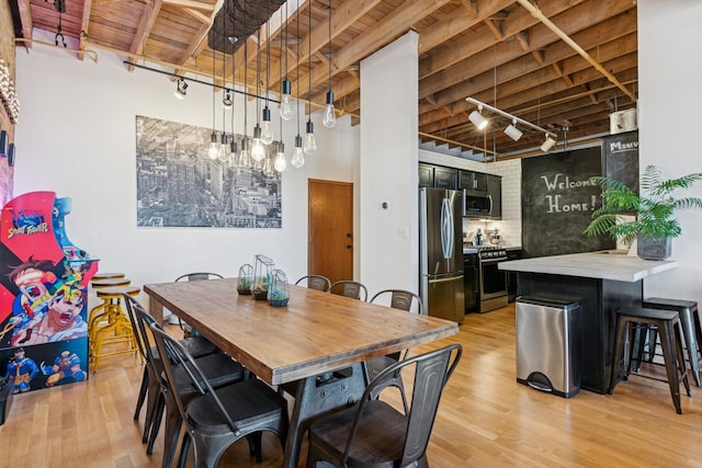 dining area featuring beam ceiling, track lighting, wood ceiling, a towering ceiling, and light wood-type flooring