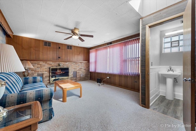 carpeted living room featuring a sink, visible vents, a brick fireplace, and a ceiling fan