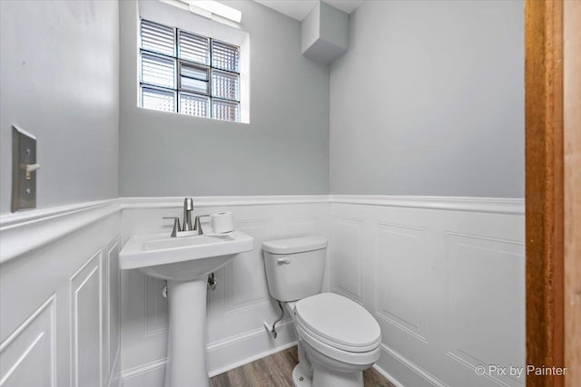 half bath with a decorative wall, toilet, wood finished floors, and wainscoting