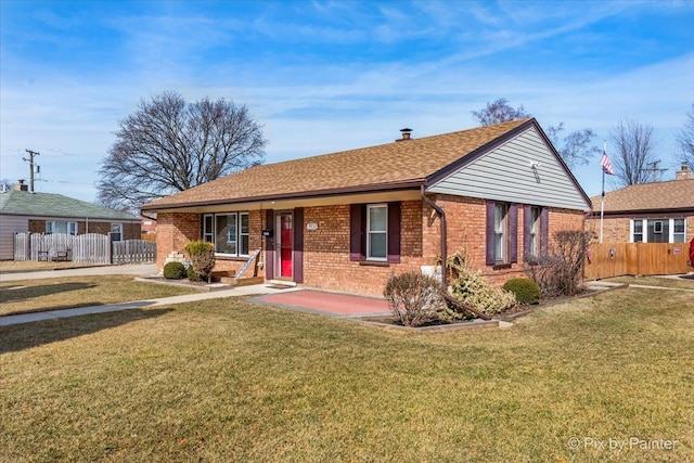 ranch-style home with a front yard, fence, brick siding, and roof with shingles